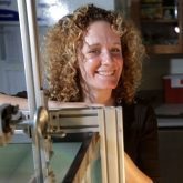 A woman with curly hair is smiling in front of a machine.
